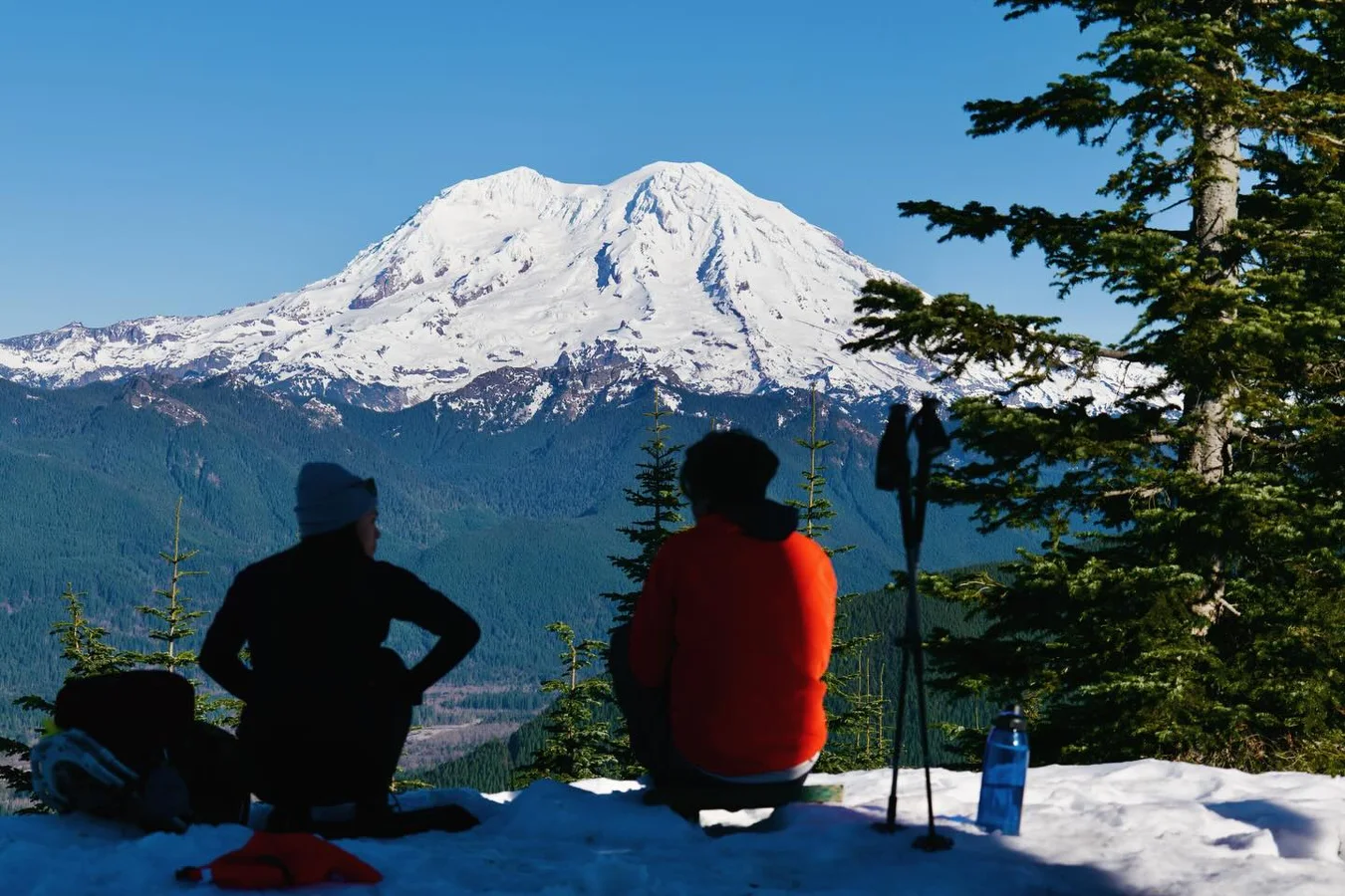 Two hikers facing Mount Rainier across the snow